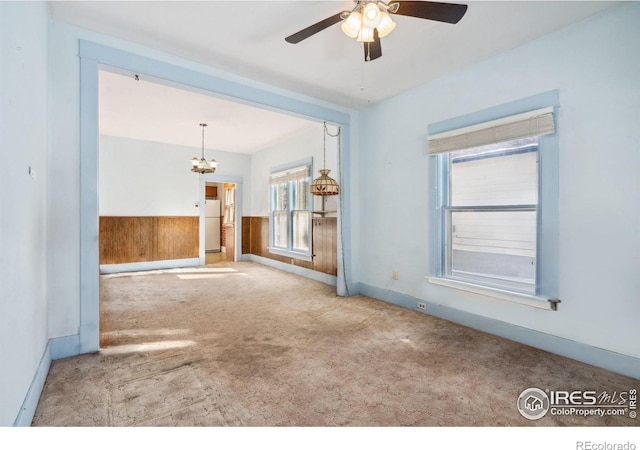 unfurnished living room with carpet flooring, ceiling fan with notable chandelier, and wood walls