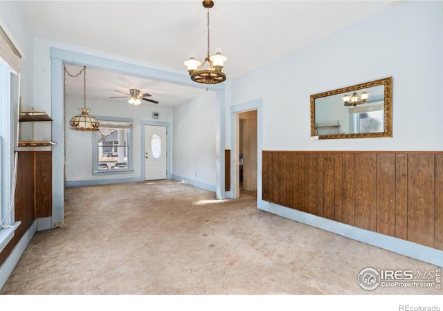 foyer entrance featuring ceiling fan with notable chandelier, wood walls, and carpet