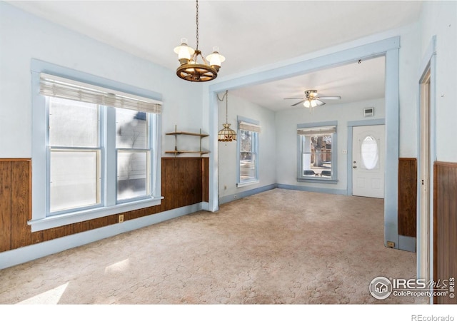 interior space with ceiling fan with notable chandelier, wooden walls, and carpet flooring