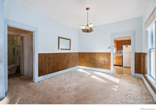 carpeted spare room with an inviting chandelier and wooden walls