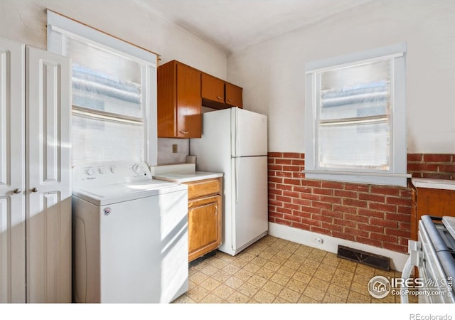 kitchen featuring white refrigerator, brick wall, and washer / dryer