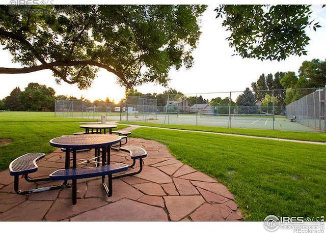 view of home's community with a tennis court, a lawn, a patio area, and fence