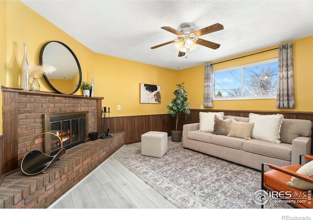 living room with a brick fireplace, wooden walls, light hardwood / wood-style floors, and ceiling fan