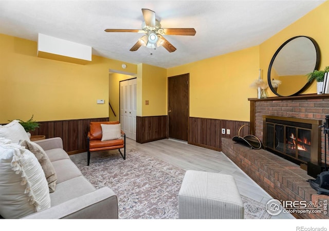 living room with a fireplace, ceiling fan, and wood walls