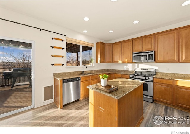 kitchen featuring appliances with stainless steel finishes, sink, a center island, light stone countertops, and light hardwood / wood-style flooring