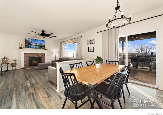 dining space featuring a brick fireplace, hardwood / wood-style flooring, and ceiling fan with notable chandelier