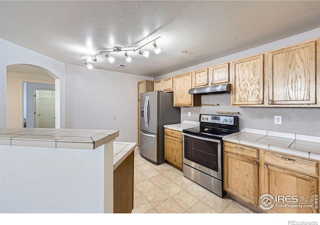 kitchen featuring stainless steel appliances, tile counters, a textured ceiling, and light brown cabinets