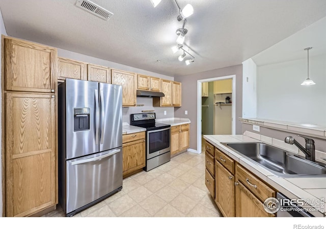 kitchen featuring decorative light fixtures, sink, stainless steel appliances, light brown cabinets, and a textured ceiling