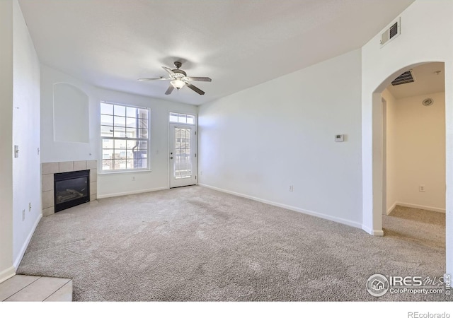 unfurnished living room featuring a tiled fireplace, light colored carpet, and ceiling fan