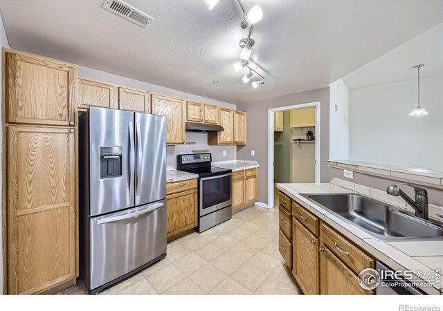 5756 N Genoa Way Unit 205, Aurora, CO 80019 - kitchen featuring stainless steel appliances, under cabinet range hood, a sink, tile countertops, and hanging light fixtures
