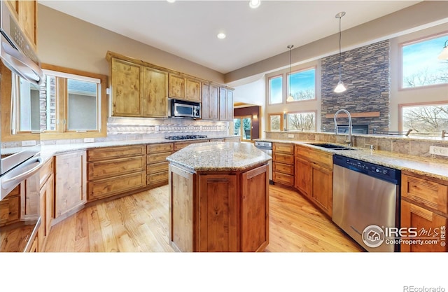 kitchen featuring sink, light stone counters, a center island, hanging light fixtures, and appliances with stainless steel finishes