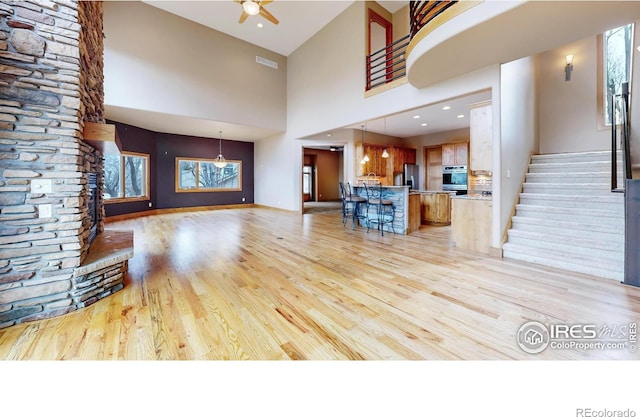 unfurnished living room with a towering ceiling, light hardwood / wood-style flooring, and ceiling fan