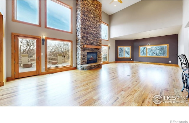 unfurnished living room with ceiling fan, a towering ceiling, a fireplace, and light hardwood / wood-style flooring