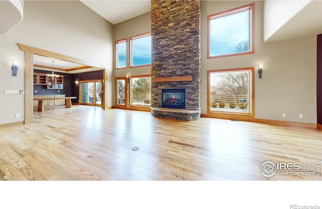 unfurnished living room featuring a fireplace, light hardwood / wood-style flooring, a chandelier, and a high ceiling