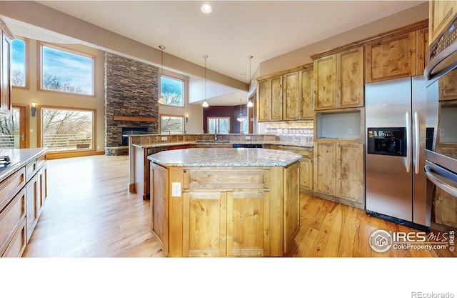 kitchen featuring hanging light fixtures, a center island, light stone counters, stainless steel fridge with ice dispenser, and kitchen peninsula