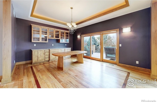 interior space with a raised ceiling, a chandelier, and light hardwood / wood-style flooring