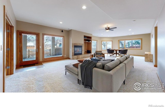 carpeted living room with ceiling fan and a tiled fireplace