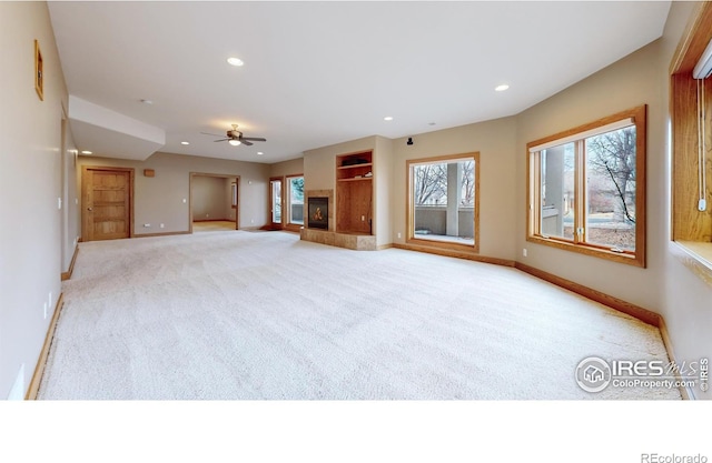 unfurnished living room featuring ceiling fan, a tile fireplace, and light carpet