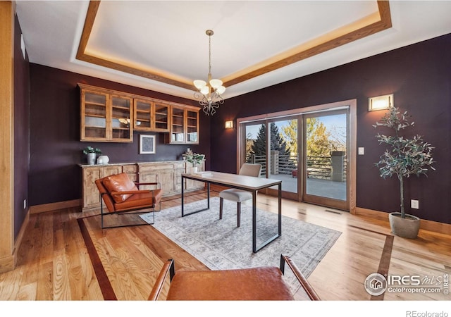 office area featuring light wood finished floors, a tray ceiling, baseboards, and an inviting chandelier