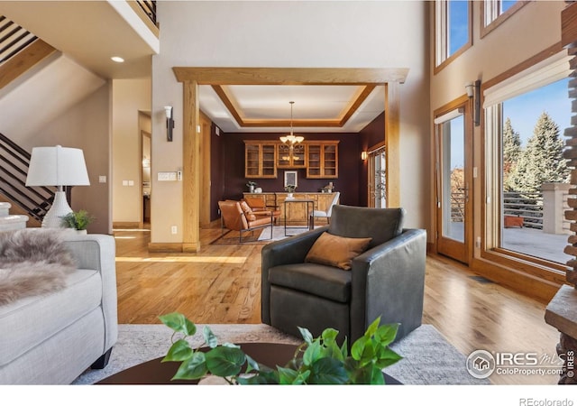 living area featuring a towering ceiling, stairway, a tray ceiling, light wood-type flooring, and a notable chandelier