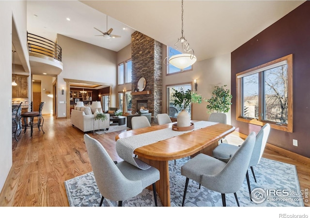 dining area with ceiling fan, a stone fireplace, light wood-style flooring, recessed lighting, and a high ceiling