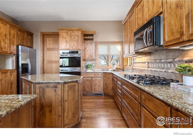 kitchen featuring wood finished floors, appliances with stainless steel finishes, brown cabinetry, and backsplash