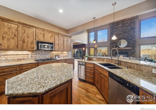 kitchen with tasteful backsplash, brown cabinetry, stainless steel appliances, a stone fireplace, and a sink