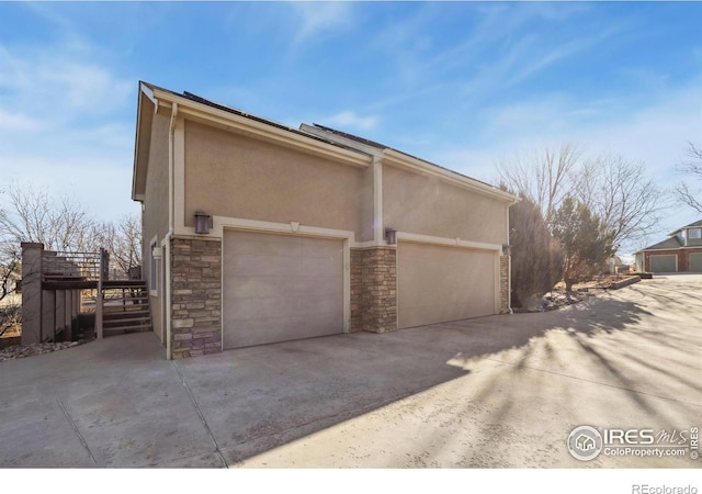 view of side of home with driveway, stone siding, and stucco siding