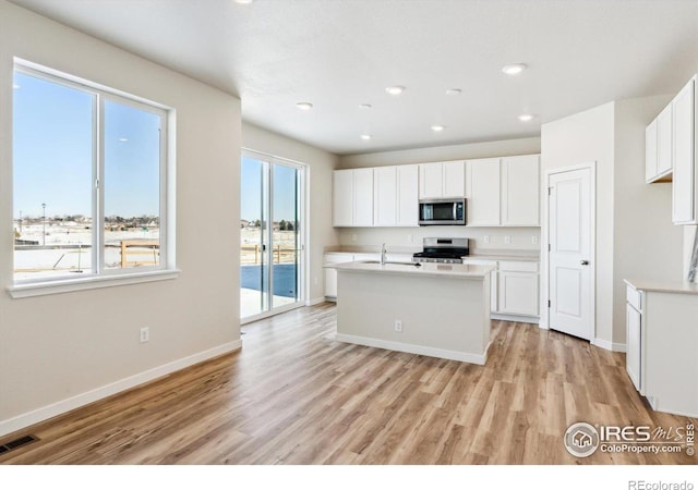 kitchen with stainless steel appliances, an island with sink, white cabinets, and light wood-type flooring