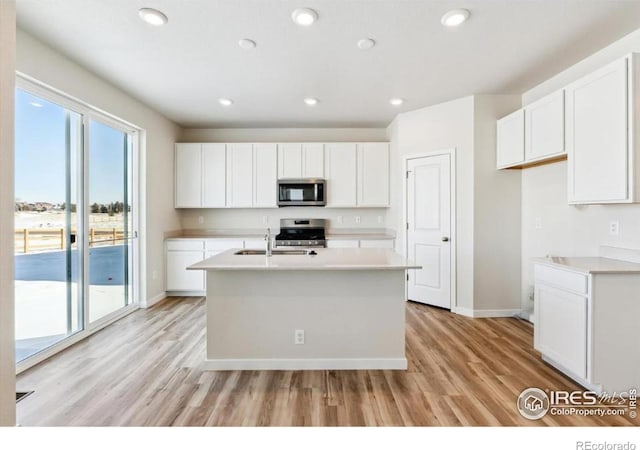 kitchen featuring sink, light wood-type flooring, appliances with stainless steel finishes, a kitchen island with sink, and white cabinets