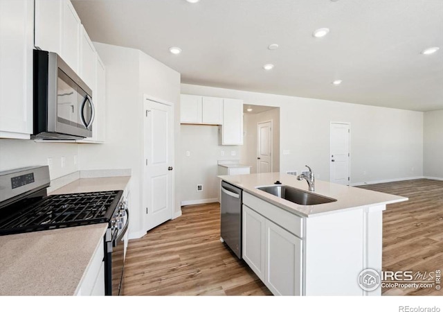 kitchen with sink, light hardwood / wood-style flooring, appliances with stainless steel finishes, white cabinets, and a center island with sink