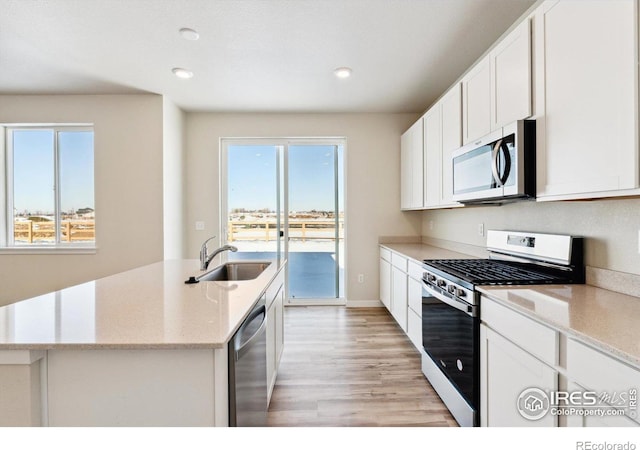 kitchen featuring sink, appliances with stainless steel finishes, white cabinetry, light stone countertops, and a center island with sink