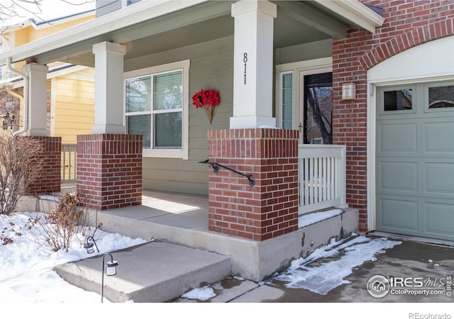 snow covered property entrance with a porch and a garage