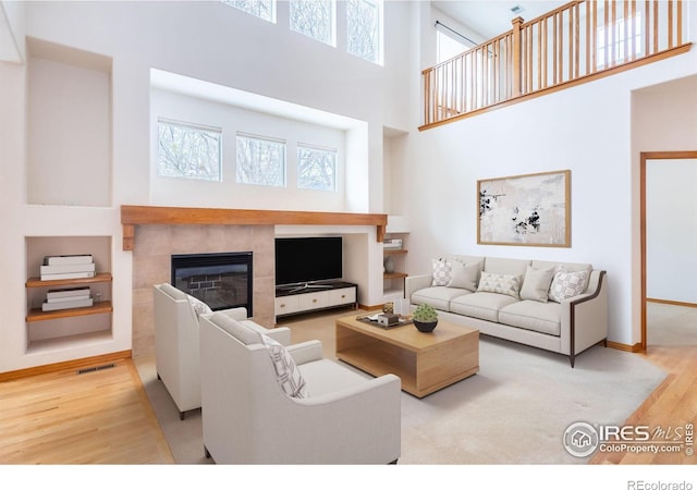 living room featuring a tiled fireplace, a towering ceiling, and light hardwood / wood-style flooring