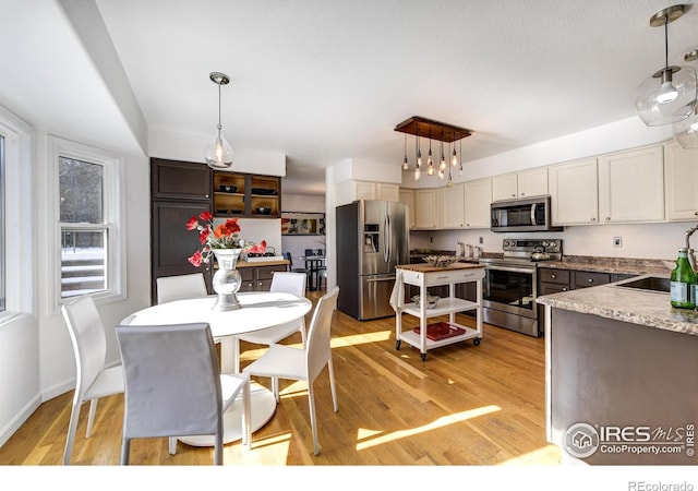 kitchen with pendant lighting, sink, stainless steel appliances, and light hardwood / wood-style floors