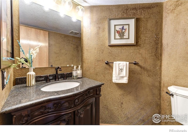 bathroom with vanity, toilet, and a textured ceiling