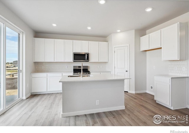 kitchen with appliances with stainless steel finishes, a center island with sink, and white cabinets