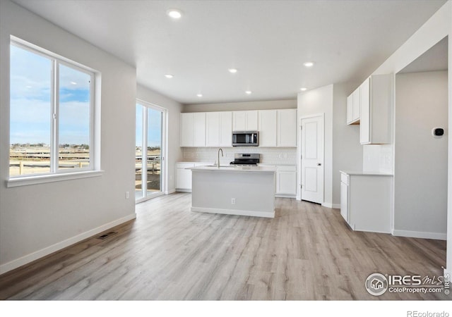 kitchen featuring light hardwood / wood-style flooring, a center island with sink, appliances with stainless steel finishes, decorative backsplash, and white cabinets