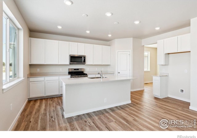 kitchen with sink, light wood-type flooring, appliances with stainless steel finishes, a kitchen island with sink, and white cabinets