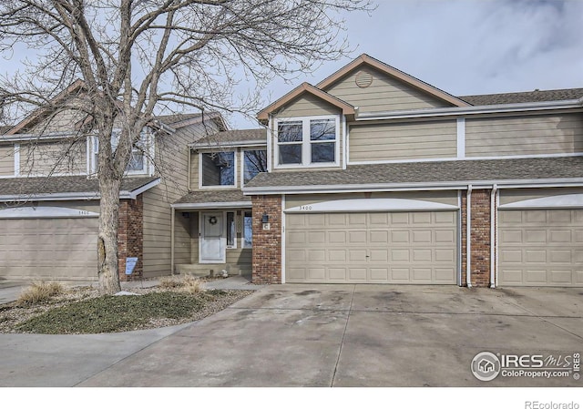 multi unit property featuring a garage, roof with shingles, concrete driveway, and brick siding