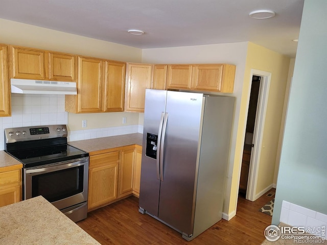 kitchen featuring light countertops, light brown cabinetry, appliances with stainless steel finishes, dark wood-type flooring, and under cabinet range hood