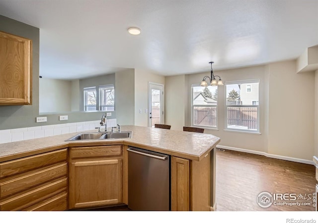 kitchen featuring light countertops, hanging light fixtures, stainless steel dishwasher, a sink, and a peninsula