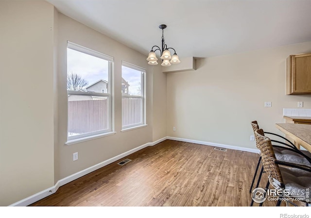 unfurnished dining area with a notable chandelier, light wood-style flooring, visible vents, and baseboards