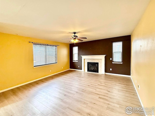 unfurnished living room with ceiling fan, a tiled fireplace, and light wood-type flooring