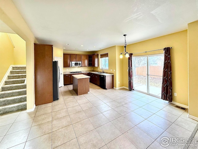 kitchen with pendant lighting, appliances with stainless steel finishes, a kitchen island, and light tile patterned floors