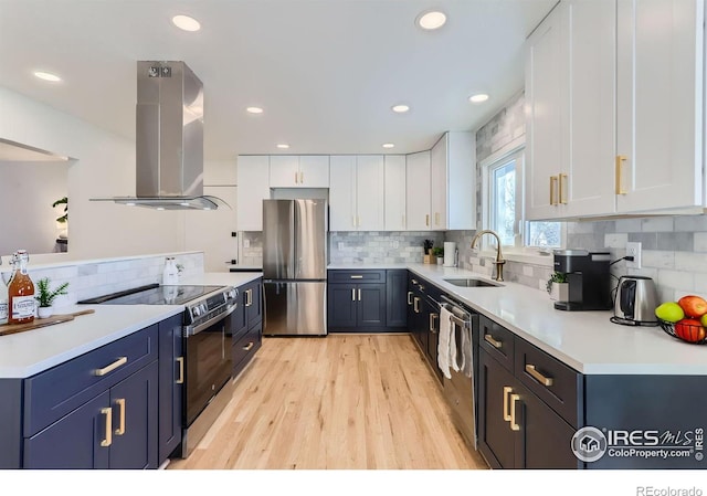 kitchen with appliances with stainless steel finishes, island range hood, white cabinetry, sink, and blue cabinetry