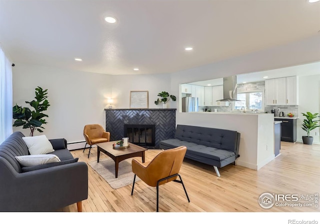 living room featuring a tile fireplace, a baseboard heating unit, and light hardwood / wood-style floors