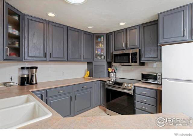 kitchen with sink, gray cabinetry, light tile patterned floors, stainless steel appliances, and decorative backsplash