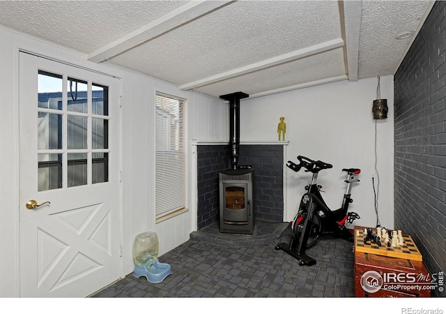 workout room with brick wall, a wood stove, and a textured ceiling