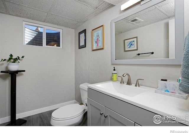 bathroom with hardwood / wood-style flooring, a paneled ceiling, vanity, and toilet